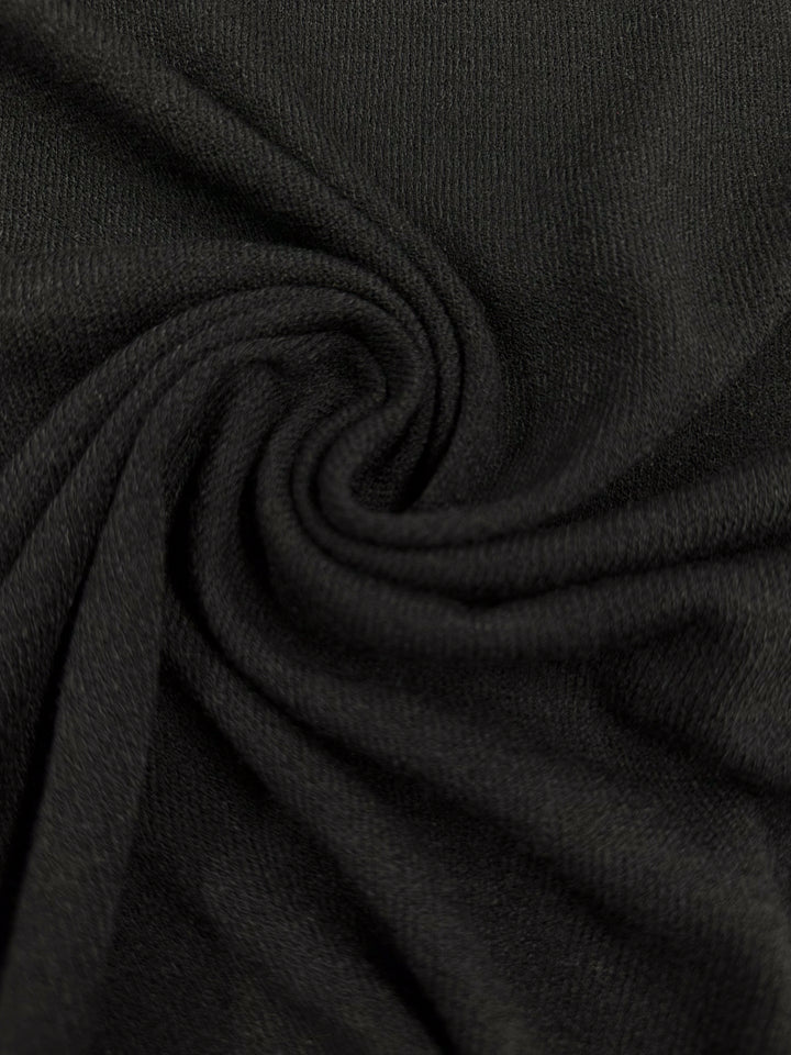 Close-up of the Textured Knit - Black fabric from Super Cheap Fabrics. This medium-weight material showcases a swirling pattern, appearing soft and textured with delicate folds around the central twist. The lighting accentuates the intricate weave details, making it ideal for elegant dresses.