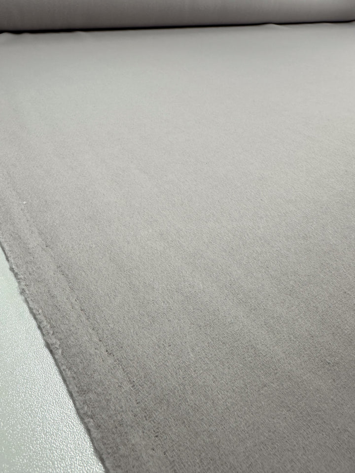 A close-up of Super Cheap Fabrics' Wool Cashmere - Gray Morn - 150cm shows its smooth, light gray heavy weight texture, luxurious softness, and the unfinished edge along the left side.