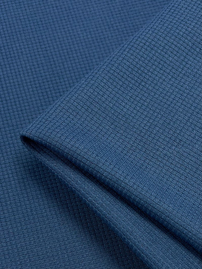 Close-up of the Super Cheap Fabrics Waffle Knit - Stellar - 170cm, showcasing its detailed weaves and soft appearance. The material appears folded, highlighting the depth and flexibility of the fabric. The consistent and uniform blue color across the folds accentuates its three-dimensional effect.