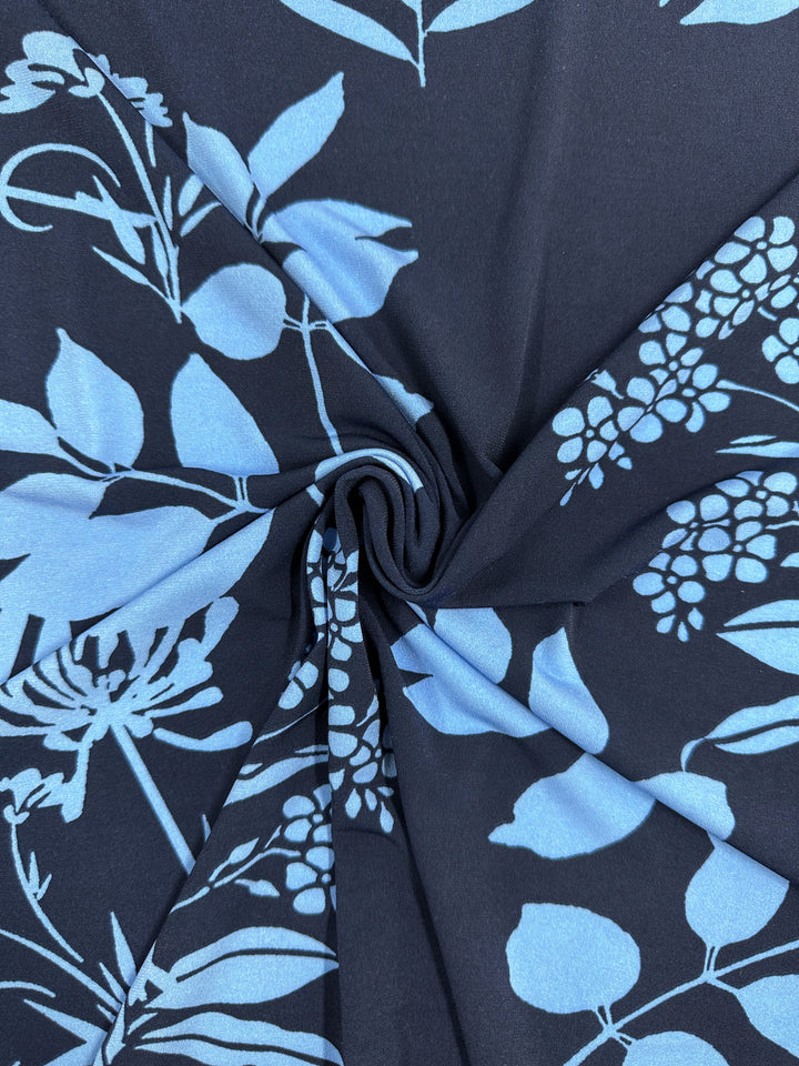 A close-up of Super Cheap Fabrics’ Printed Lycra - Silhouette Garden (150cm), a medium-weight polyester spandex with a light blue botanical print, shown twisted at the center for folds and a spiral effect.