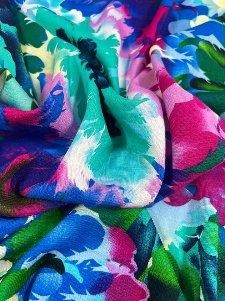 A close-up photo of a colorful, crumpled fabric with a vibrant floral pattern. The design, made from versatile clothing materials including Super Cheap Fabrics Designer Bamboo Rayon - Lantana - 147cm, consists of various shades of blue, pink, green, and turquoise, blending together to create a lively and dynamic look.