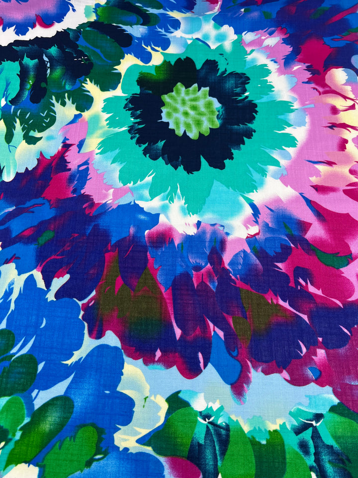 A vibrant, tie-dye style pattern on Designer Bamboo Rayon - Lantana - 147cm by Super Cheap Fabrics featuring a mix of bright blue, green, pink, purple, and white colors. The design includes abstract, flower-like shapes radiating from a central green and blue area, creating an intricate, eye-catching display perfect for versatile clothing.