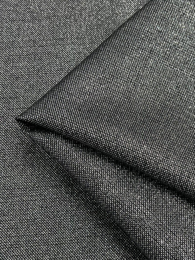 A close-up of dark gray fabric with a visible weave pattern. The Wool Lamé - Metallic - 150cm by Super Cheap Fabrics appears to be folded diagonally, showcasing its texture and thickness. The material has a slightly shiny, speckled appearance, indicating a blend of fibers.