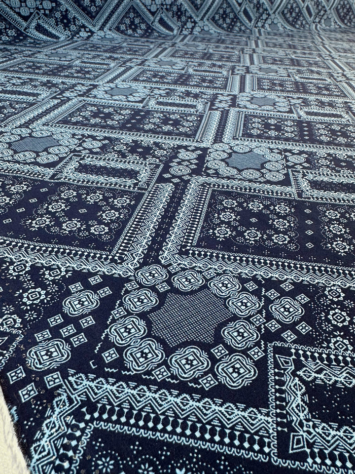 A close-up of Super Cheap Fabrics' Designer Rayon - Navy Nomad (145cm) shows dark blue fabric with intricate white geometric and floral patterns in a symmetrical, repeating design. The versatile fabric displays vibrant prints and is spread flat.