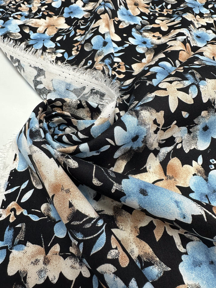 A close-up of Super Cheap Fabrics’ Designer Rayon - Dusty Petals (145cm) shows its lightweight texture, subtle frayed edge, and floral print in blue, beige, and white.