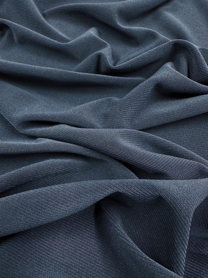 Super Cheap Fabrics’ ITY Knit - Denim - 150cm features dark blue polyester spandex with a textured surface and soft, irregular folds that create a flowing, wavy pattern on this medium weight fabric.