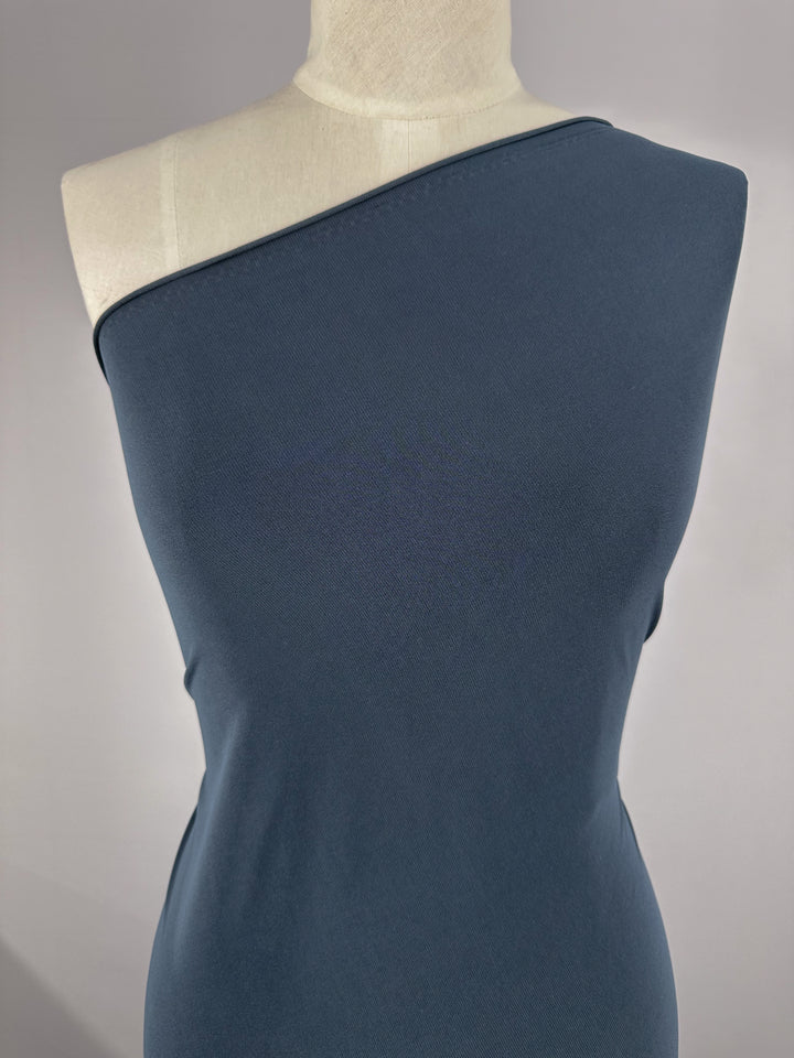 A mannequin wears a fitted, one-shoulder dress made from Super Cheap Fabrics' ITY Knit - Denim (150cm), a medium-weight polyester spandex, against a plain light background.