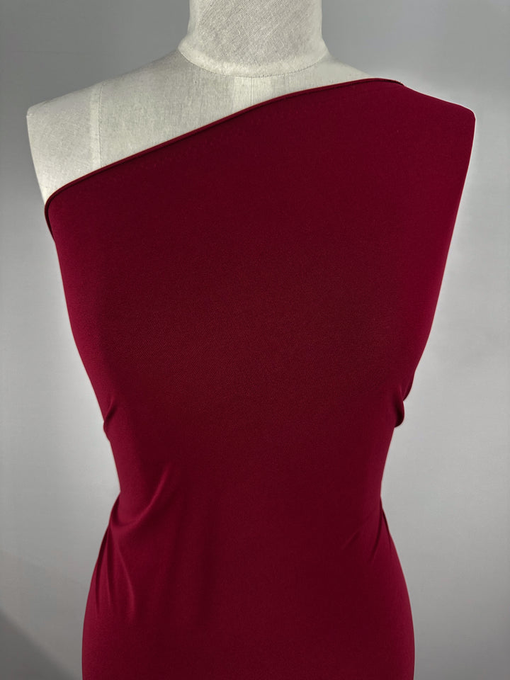 A torso mannequin showcases a fitted, one-shoulder dress made from Super Cheap Fabrics’ ITY Knit - Red Bud (150cm), featuring medium weight and a smooth feel, set against a plain gray background.