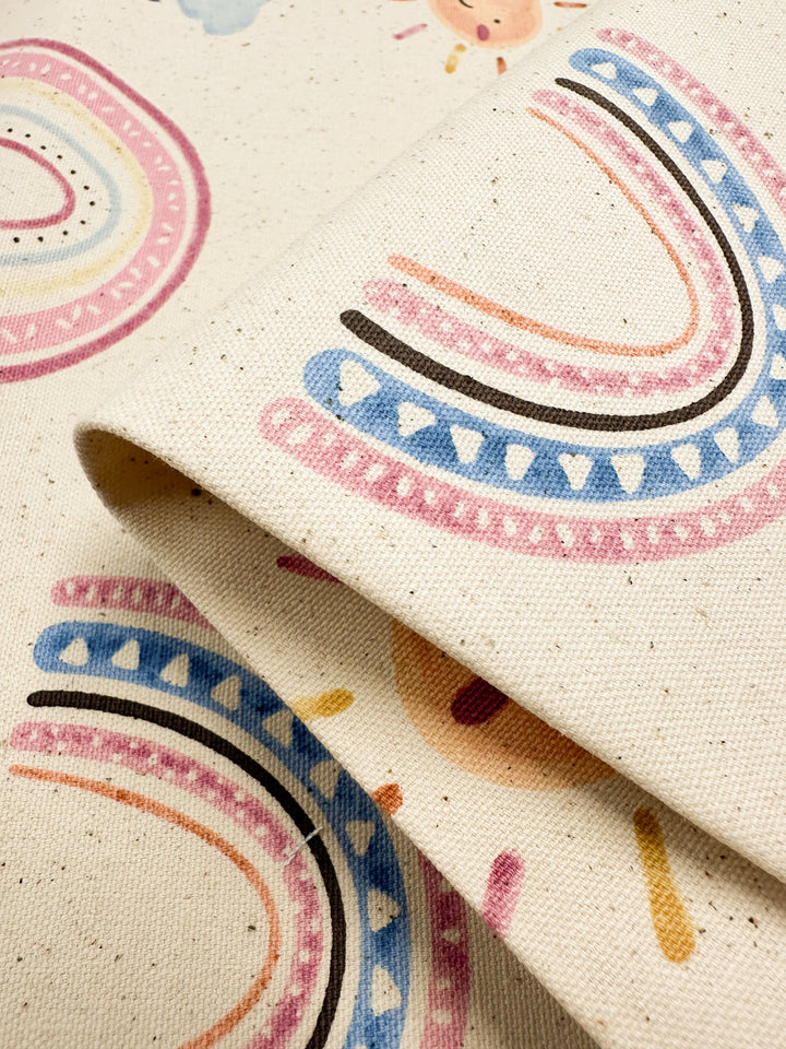 A close-up view of the Cotton Duck - Rainbow Natural fabric from Super Cheap Fabrics reveals an array of colorful abstract patterns in pastel shades of pink, blue, and black on medium-weight cotton. The design features curved and dotted elements that create a playful and artistic look, perfect for home décor. The fabric is displayed slightly folded and layered.