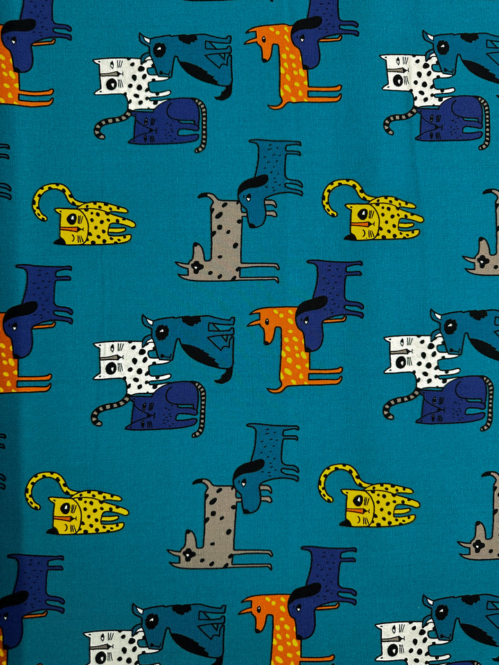 Cotton Duck - Cat Dog by Super Cheap Fabrics is a medium-weight patterned cotton fabric, showcasing cartoon animals like cats, dogs, and giraffes stacked against a teal background. The vibrant colors of yellow, orange, and blue add a playful and whimsical touch, making it perfect for home décor projects.