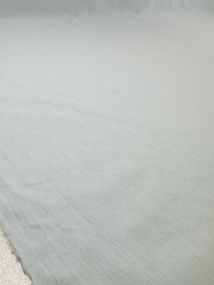 A close-up of Super Cheap Fabrics’ Textured Cotton - Ice Melt (145cm) shows its pale gray color and subtle texture, softly lit to highlight gentle folds and surface details.