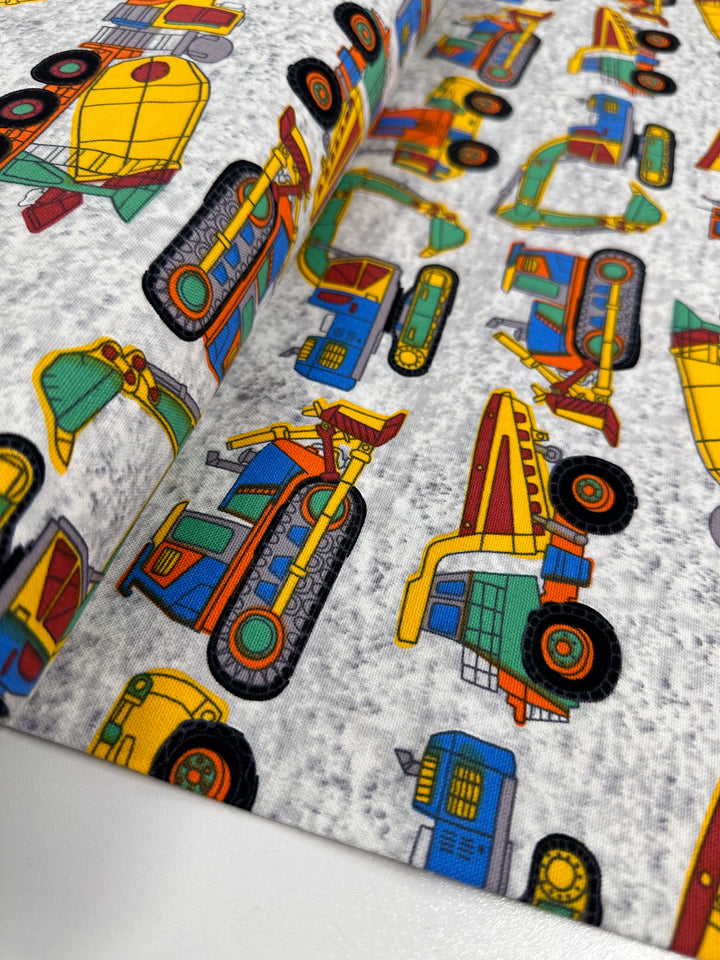 Super Cheap Fabrics presents "Cotton Duck - Construction - 112cm," a vibrant cotton fabric showcasing images of construction vehicles like trucks and bulldozers on a gray backdrop. Ideal for home décor projects, its medium weight adds a whimsical element to any room.