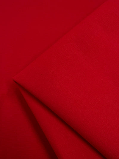 Close-up image of vibrant red fabric with a smooth texture. The cloth is folded neatly, showcasing clean lines and a rich, uniform color. This stretch fabric appears soft and slightly shiny, emphasizing its high-quality finish. This is the Milano Ponte - Red - 165cm from Super Cheap Fabrics.