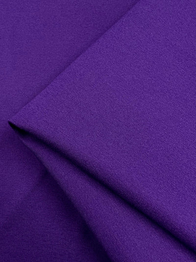 A close-up image of Super Cheap Fabrics' Milano Ponte in Violet Indigo, featuring a smooth texture. The 165cm wide, heavy weight fabric is neatly folded, showcasing its rich color and fine weave.