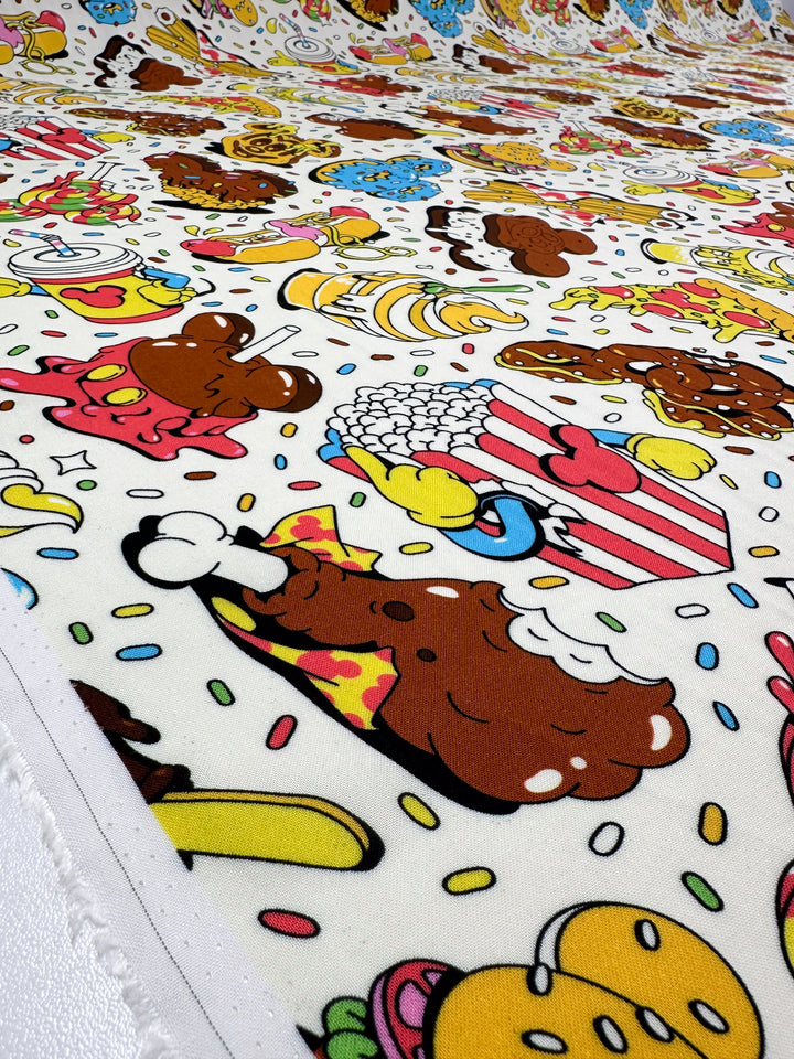 The Printed Rayon - Treat - 140cm by Super Cheap Fabrics features a vibrant pattern of cartoon-style illustrations of cheeseburgers, pizza slices, popcorn, and ice cream cones playfully surrounded by sprinkles on a versatile rayon background.