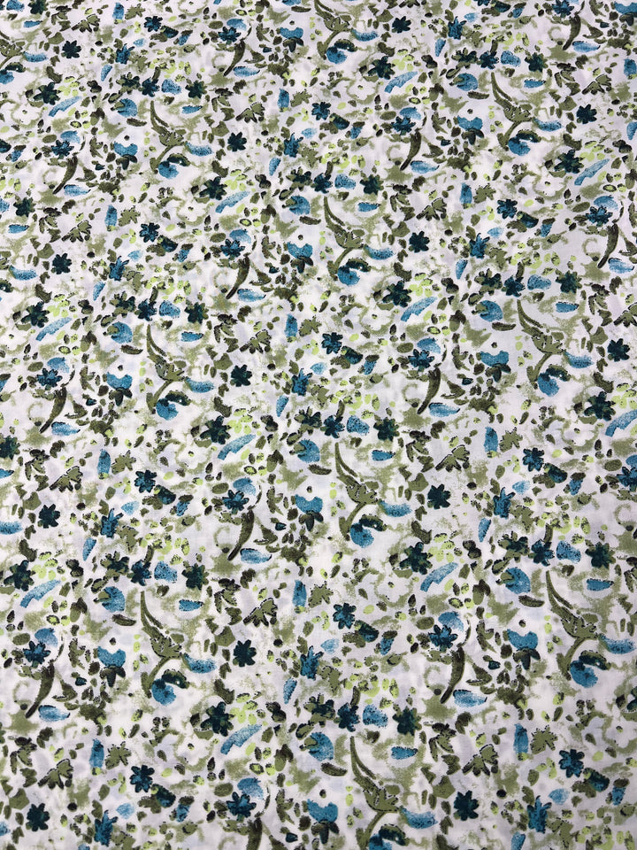 Introducing the Printed Cotton - Blue Natures Mark - 148cm by Super Cheap Fabrics: a lightweight, 100% cotton fabric adorned with an intricate floral pattern. It features small flowers and leaves in vibrant shades of blue, green, and brown on a crisp white background. This densely packed design creates a beautifully textured look.