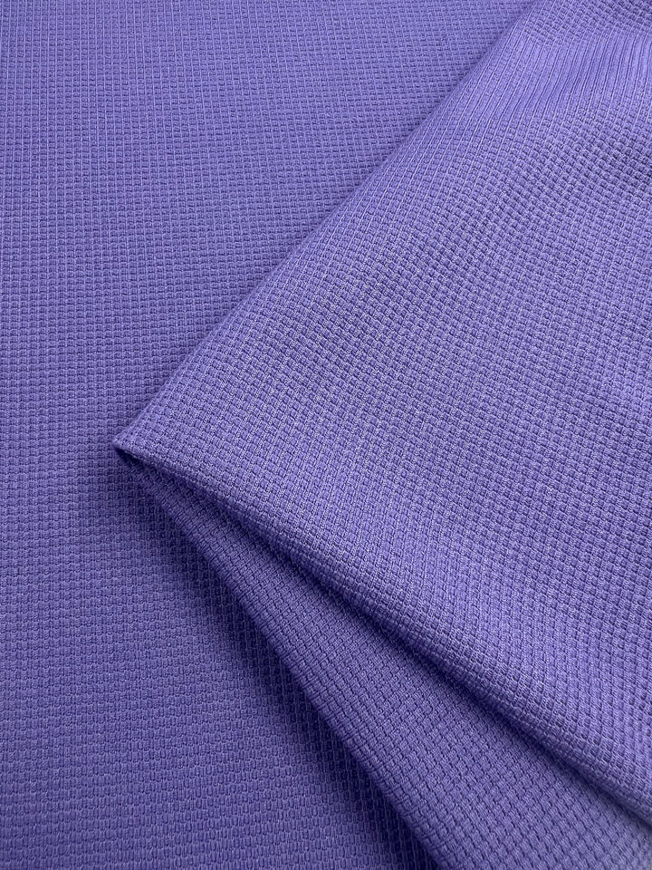 Close-up of a folded piece of Waffle Knit - Sunlit Allium - 170cm from Super Cheap Fabrics, featuring a textured, waffle-like pattern. The honeycomb fabric appears to be soft and evenly woven, with one edge neatly folded over the rest. The surface has a subtle sheen, highlighting the fine details of its three-dimensional appearance.