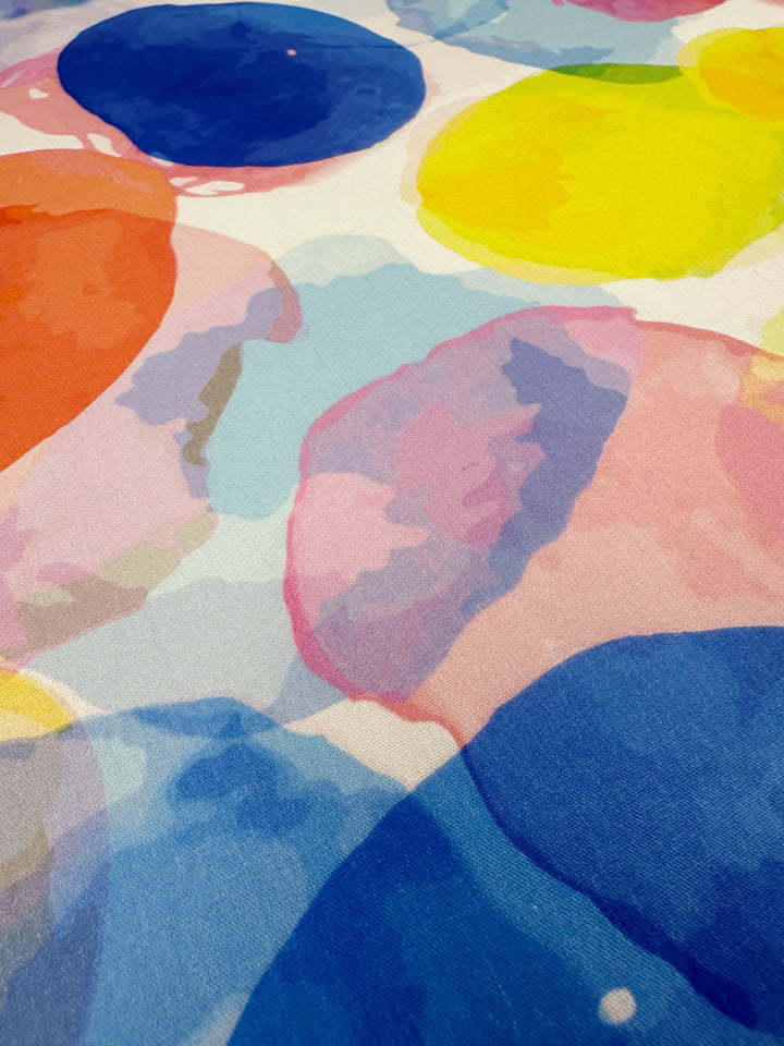 This printed cotton fabric from Super Cheap Fabrics, named "Bubble," features a vibrant abstract pattern of overlapping circles in blue, yellow, pink, orange, and purple. With its textured surface and natural cotton fibers, it's ideal for crafting unique clothing and household items. The fabric measures 150cm in width.