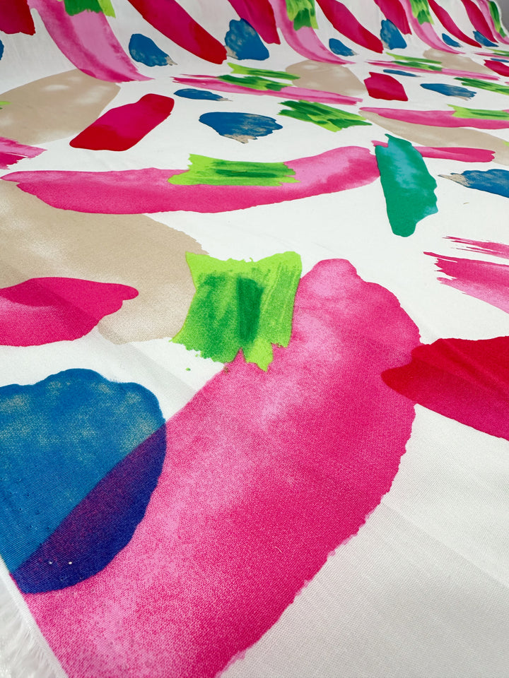 This energetic and lively design, reminiscent of a colorful abstract painting, presents an array of bold brush strokes in pink, red, green, blue, and beige on a white background. Ideal for home decor applications, the "Printed Cotton - Salada - 150cm" by Super Cheap Fabrics captures intricate layering that evokes the texture of printed cotton fabric.