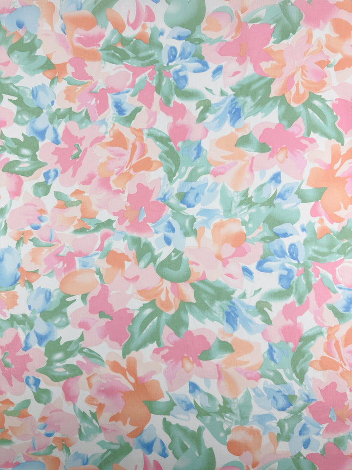 The "Printed Cotton - Blossoms - 150cm" from Super Cheap Fabrics showcases a vibrant floral pattern with abstract shapes in pink, orange, green, and blue hues, offering a lively and colorful design with versatile multiuses.