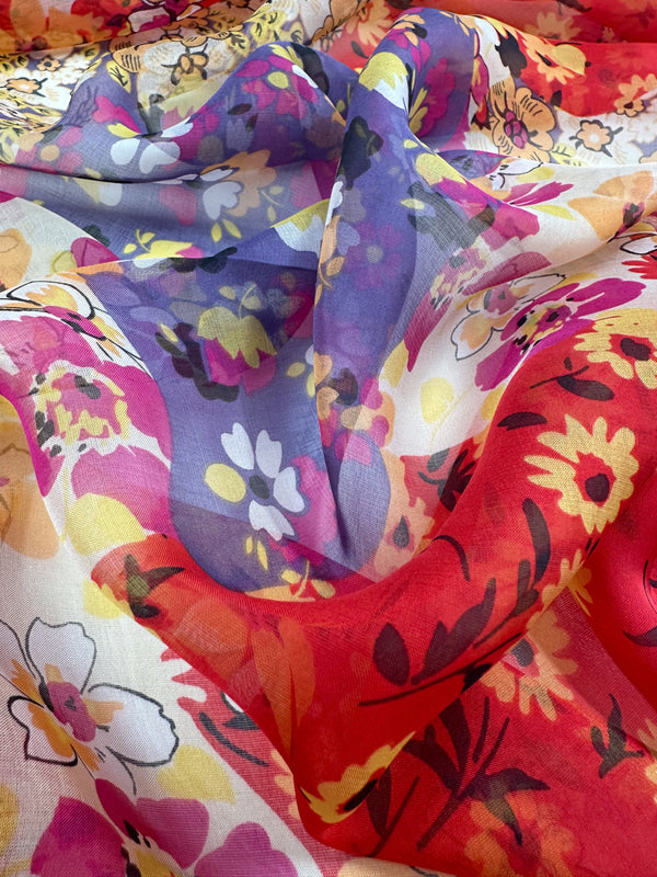 A detailed view of the Printed Silk - Florazard - 140cm by Super Cheap Fabrics reveals a spectrum of vibrant floral patterns intertwined in red, yellow, purple, and white hues. This extra lightweight material boasts a sheer and delicate quality, ideal for creating elegant dresses with its vivid and intricate designs.