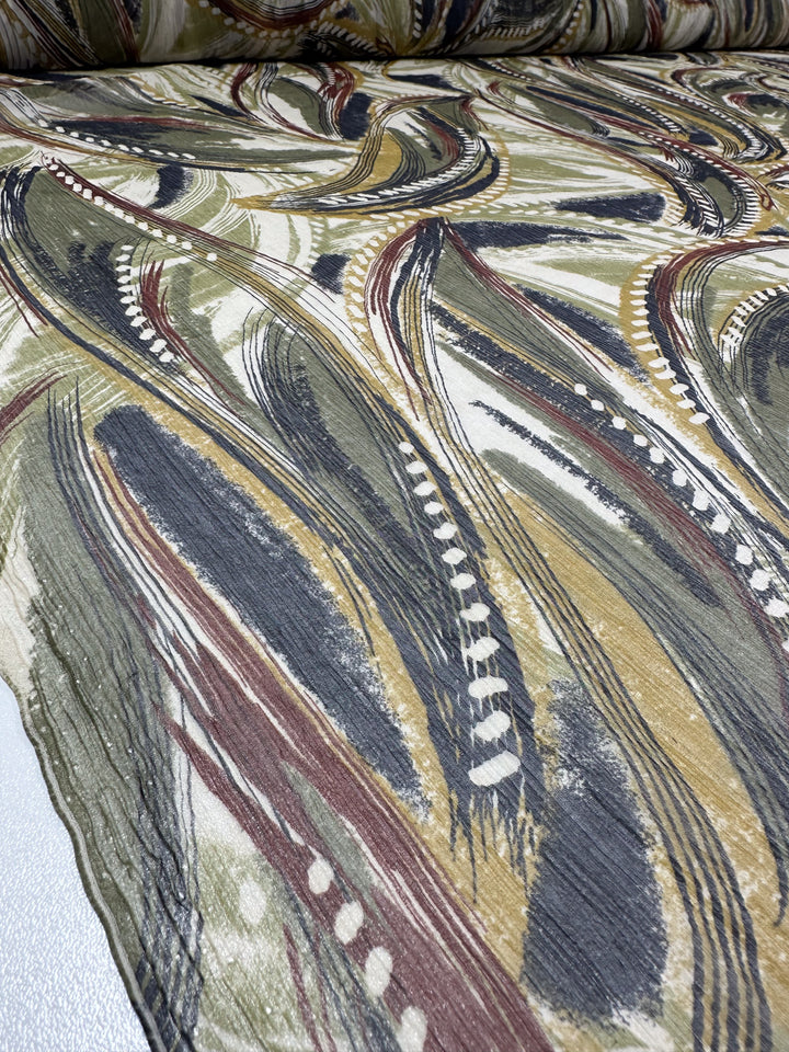 Close-up of the Pure Printed Silk - Feathers by Super Cheap Fabrics, highlighting its abstract pattern with brushstroke designs in green, mustard, black, and white. The slightly crinkled texture showcases a dynamic and artistic aesthetic reminiscent of embroidery elegance.