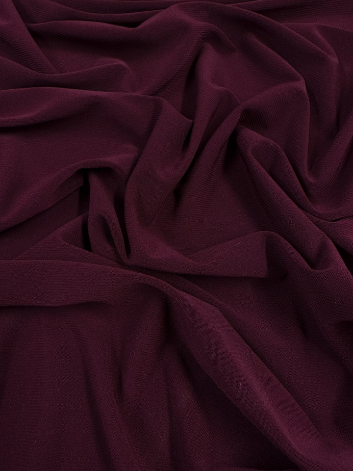 A close-up of the ITY Knit - Merlot - 150cm from Super Cheap Fabrics reveals its soft, textured surface with gentle folds and drapes. The rich color and smooth polyester spandex composition contribute to an elegant and plush appearance.