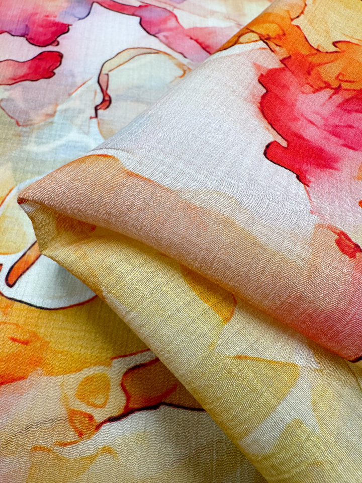 A close-up of a folded piece of Super Cheap Fabrics' Designer Cotton - Flintstones - 150cm highlights a vibrant watercolor pattern with shades of pink, orange, and yellow. Ideal for luxury sewing projects, the abstract design features fluid shapes that seamlessly blend into each other.