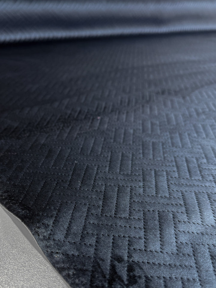 Close-up of Embossed Velvet - Oceana - 150cm by Super Cheap Fabrics, featuring a dark, heavy quilted zigzag pattern with a soft sheen and textured finish. A flat metallic edge appears in the lower left corner.