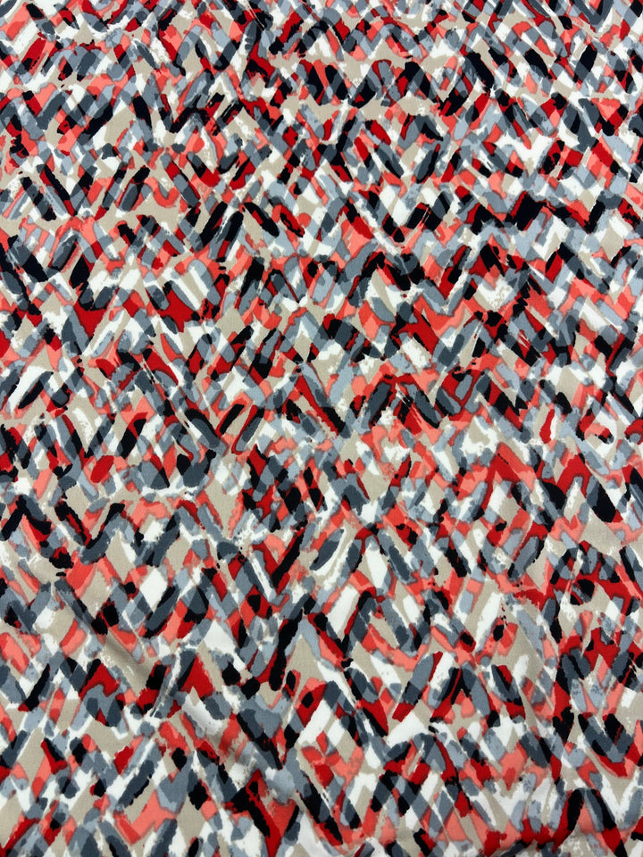 A close-up view of Super Cheap Fabrics' Printed Lycra - Stroke - 150cm, showcasing an abstract pattern with interwoven, irregular shapes in shades of red, black, gray, and white. The design features dynamic, overlapping strokes creating a textured, layered appearance on this medium-weight fabric.