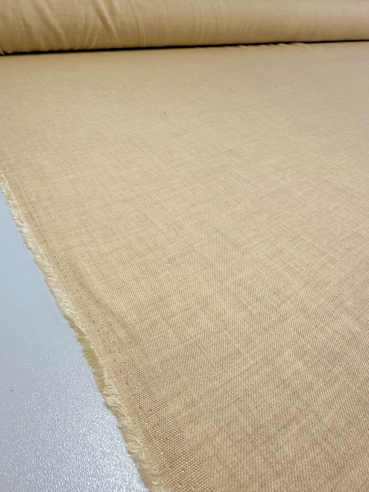 A close-up view showcases a large roll of the "Linen Blend - Banana Crepe - 142cm" fabric from Super Cheap Fabrics, unwinding on a flat surface. The lightweight material exhibits a soft and even weave, with slightly frayed edges visible on the left side of the image.