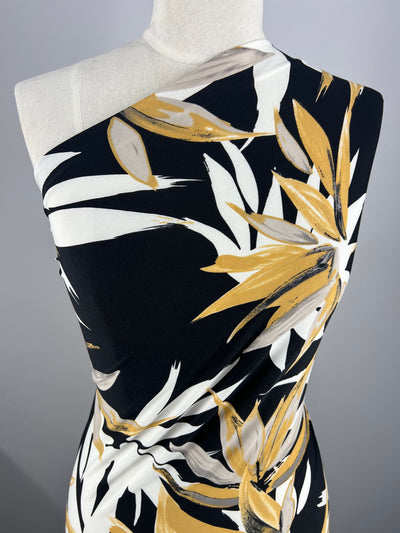 Close-up of a mannequin showcasing a one-shoulder dress made from Super Cheap Fabrics' Printed Lycra - Bamboo - 150cm. The eye-catching floral design displays large yellow and white flowers against a black backdrop, providing a striking contrast with the medium-weight material.