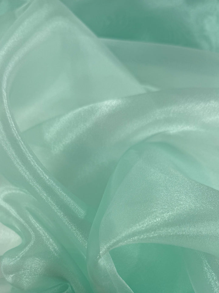 Close-up of Super Cheap Fabrics' Organza - Aqua Glass (150cm): soft, light aqua blue fabric with gentle folds and a smooth, shiny texture reflecting light, similar to sheer organza.