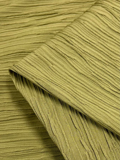 A close-up image showcases the "Textured Knit Struttra - Southern Moss - 130cm" by Super Cheap Fabrics. The medium to heavy weight knit fabric appears soft and features horizontal ridges that create a wavy, crinkled, pleated texture. Perfect for dresses in the Southern Moss shade, the corner of the fabric is slightly folded over.