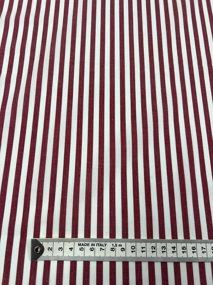 A close-up of **Super Cheap Fabrics'** lightweight **American Beauty Cotton Lawn** shows alternating vertical red and white stripes. At the bottom, a measuring tape marked in centimeters is placed horizontally, starting from 0 cm on the left and extending to 15 cm on the right. The fabric is labeled "Made in Italy," making it ideal for warm weather clothing.