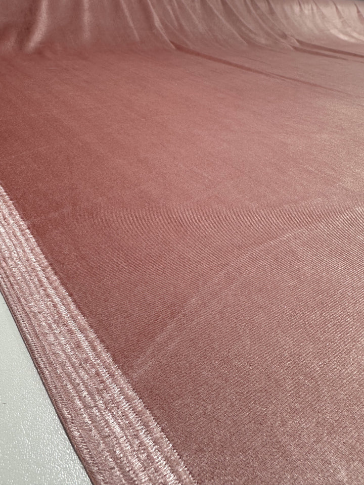 A close-up view of the smooth, shiny surface of the Peachskin Stretch Velour from Super Cheap Fabrics reveals its subtle sheen. The velvety texture feels soft and luxurious, with gentle ripples visible under the light. This fabric elegantly extends into the background, showcasing its full 160cm width.