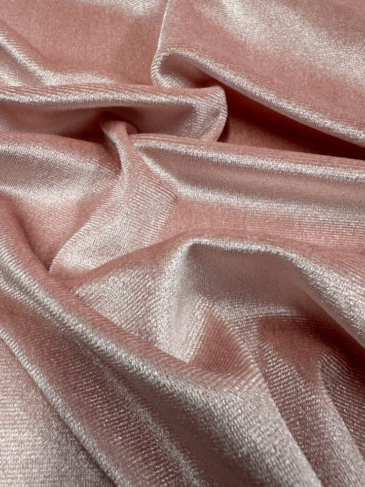 A close-up view of the Super Cheap Fabrics Stretch Velour - Peachskin - 160cm reveals its silky texture and lustrous surface, with gentle folds accentuating the soft, shimmery appearance. The fabric reflects light beautifully, highlighting its elegant sheen and luxurious finish.