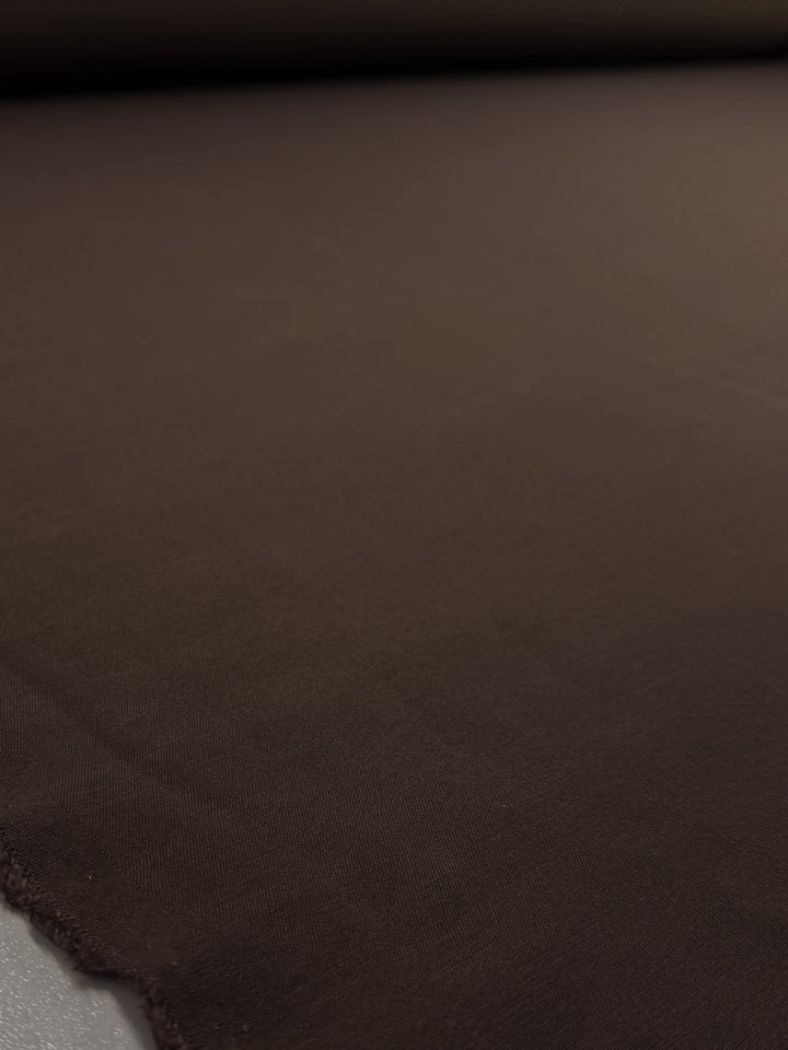 A close-up of Super Cheap Fabrics’ Cotton Bengaline in Espresso Brown (145cm), showing its smooth stretch surface laid flat with a lightly frayed edge in the lower left corner.