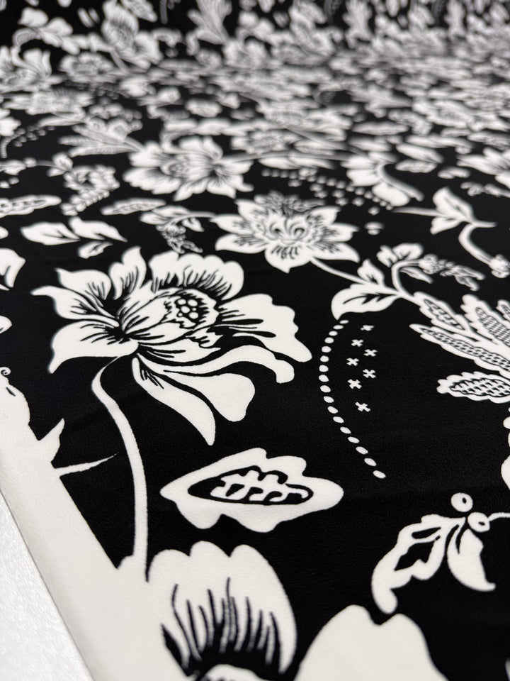Super Cheap Fabrics' Printed Lycra - Monochrome Botanica (150cm) features a bold black and white floral pattern with leaves and decorative shapes, creating an intricate design on medium-weight lycra fabric.