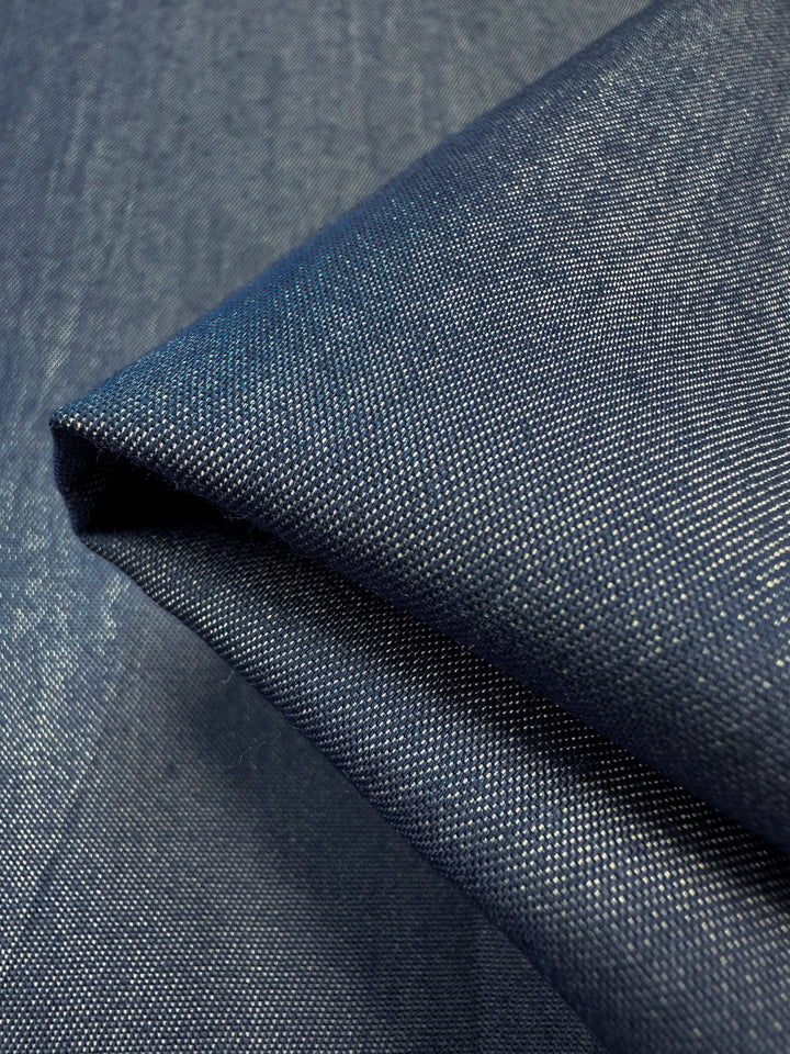 Close-up of the folded Chambray - Denim - 150cm fabric by Super Cheap Fabrics, showcasing its texture and weave. This lightweight fabric features a classic, slightly glossy appearance with visible diagonal lines, emphasizing its durable and stylish nature.