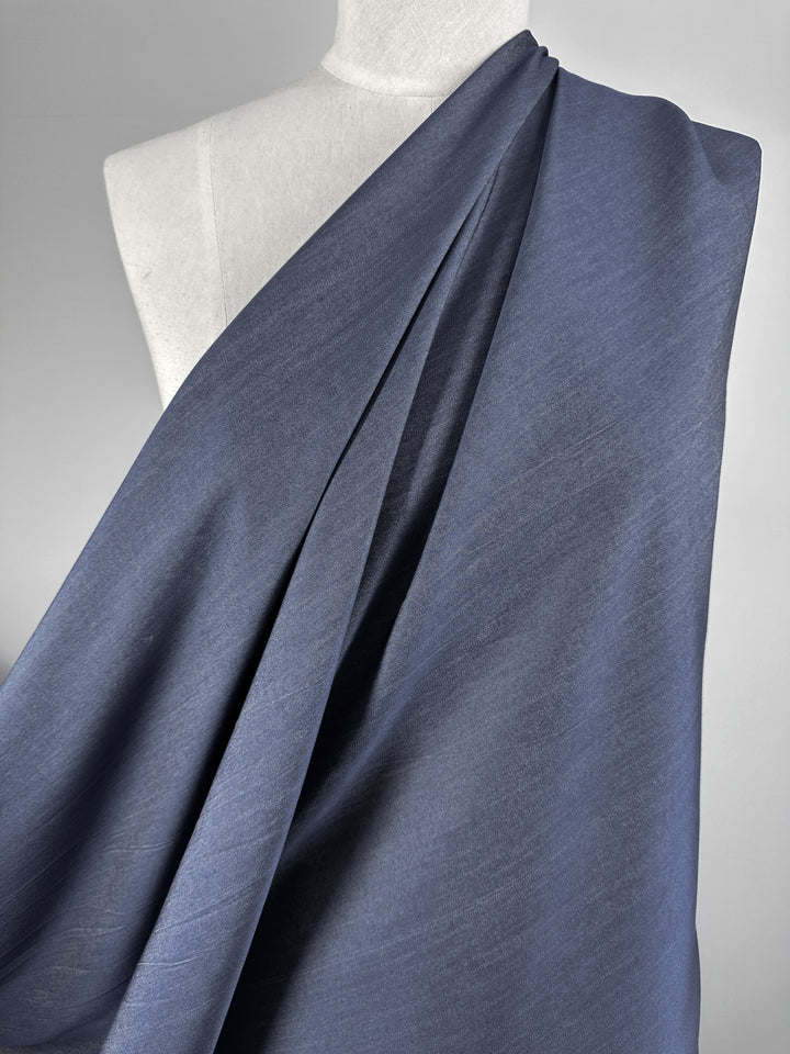 A mannequin adorned in Super Cheap Fabrics' Chambray - Denim - 150cm, showcasing the fabric's soft texture as it elegantly falls over the shoulder. The lightweight material forms gentle folds, creating a beautiful sense of flow against a neutral gray backdrop.