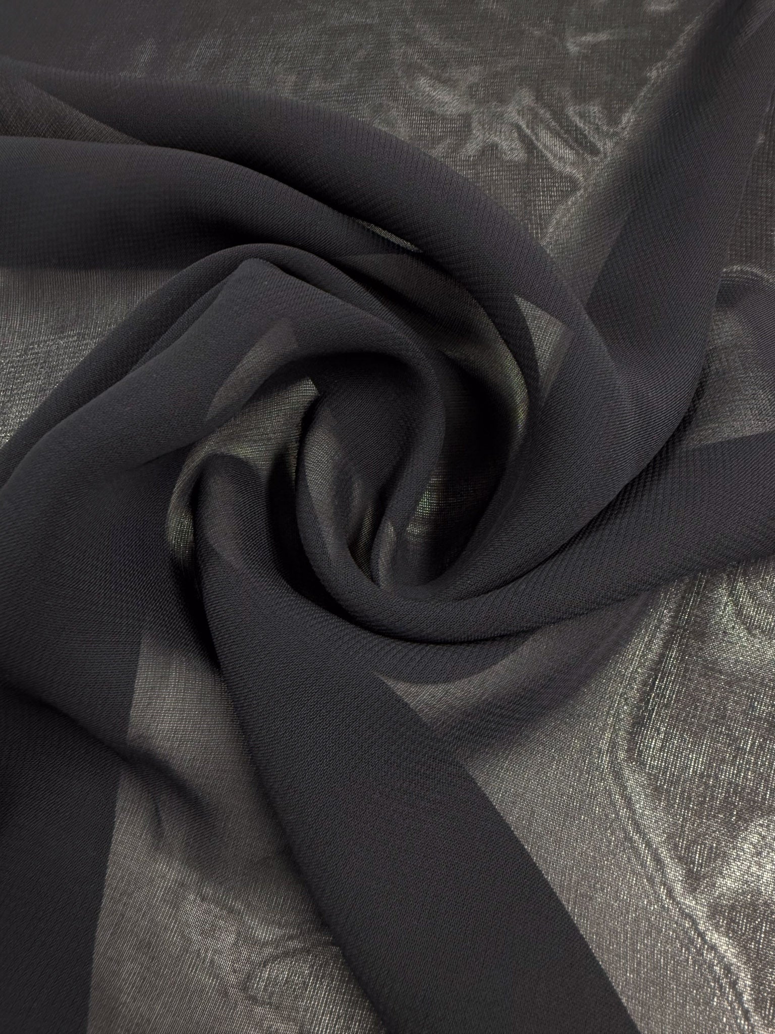 A piece of Single Georgette - Darkest Navy (143cm) from Super Cheap Fabrics arranged in a loose spiral on a shiny, textured silver surface.