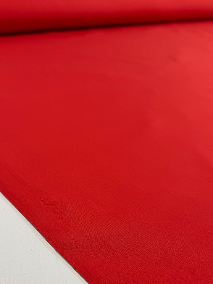 A close-up of Super Cheap Fabrics' Poplin - Signal Red (114cm) shows the fabric’s smooth texture and vibrant, solid color spread out on a flat surface.