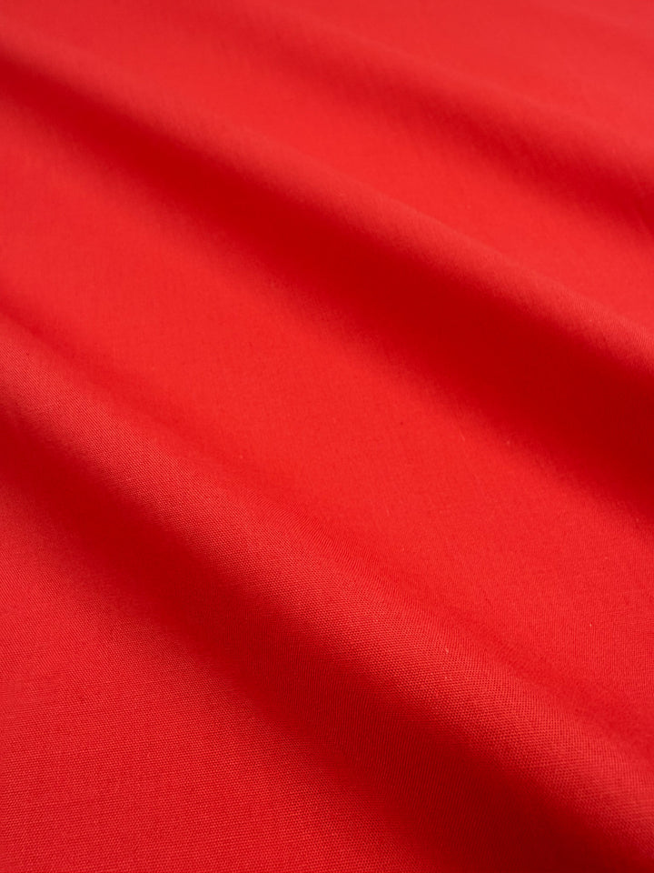 A close-up of Super Cheap Fabrics’ Poplin - Signal Red (114cm) reveals smooth, lightweight poly cotton with gentle folds and soft shadows.