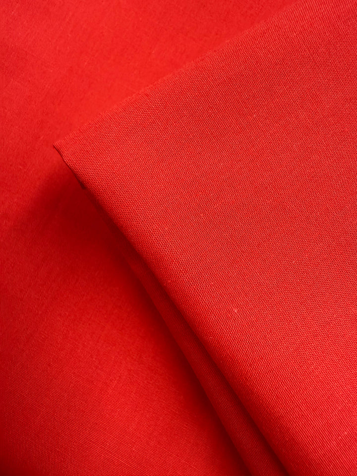A close-up of two pieces of Super Cheap Fabrics' Poplin - Signal Red (114cm) shows smooth poly cotton texture and clean edges, with one piece slightly folded over the other.