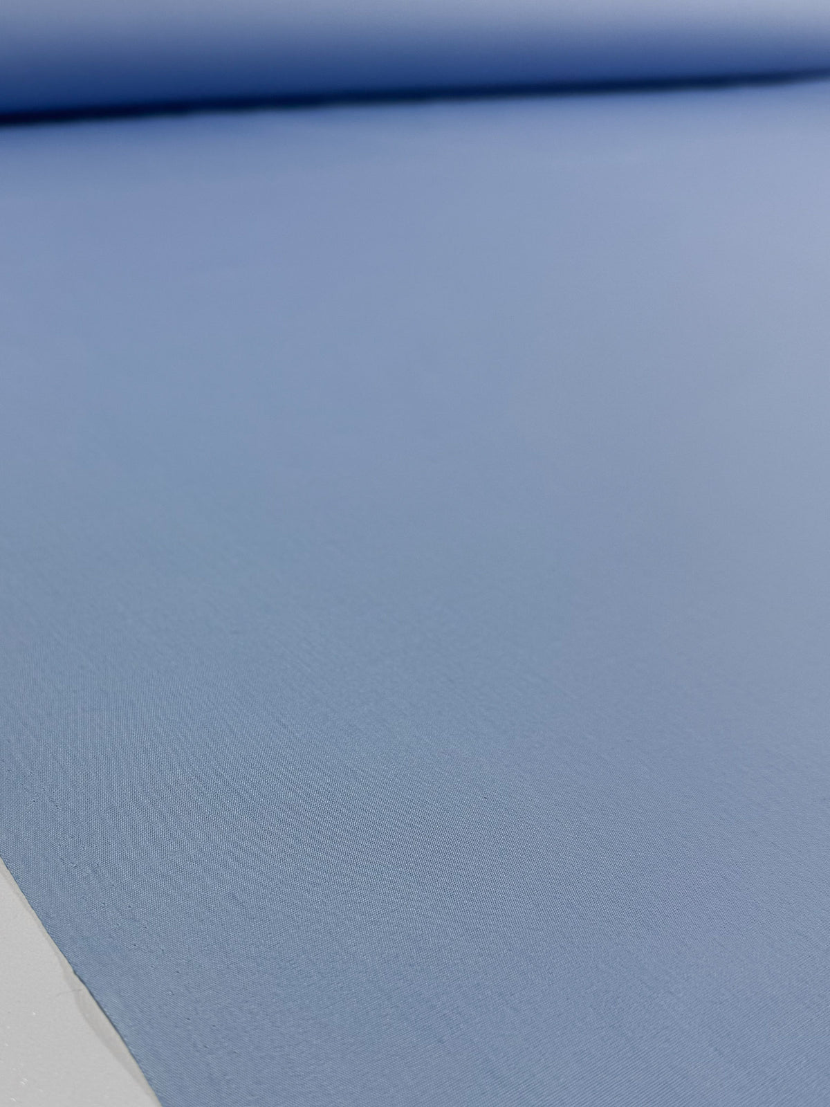 A close-up of Super Cheap Fabrics' Poplin - Powder Blue - 114cm shows the smooth, even texture of this lightweight poly cotton fabric, laid flat with a matching roll in the background.