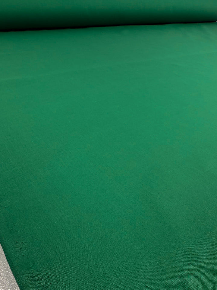 The Super Cheap Fabrics Poplin - Emerald Plain - 114cm fabric is displayed flat, highlighting its smooth, lightweight, and unpatterned surface.