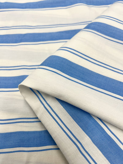 Close-up image of Super Cheap Fabrics' Linen Viscose - Blithe - 154cm, featuring lightweight material with horizontal stripes. The fabric displays alternating thick white and blue stripes separated by thin white and blue stripes. Slightly folded in one corner, it highlights its smooth texture and pattern continuity, emphasizing the elegance of the linen viscose blend.