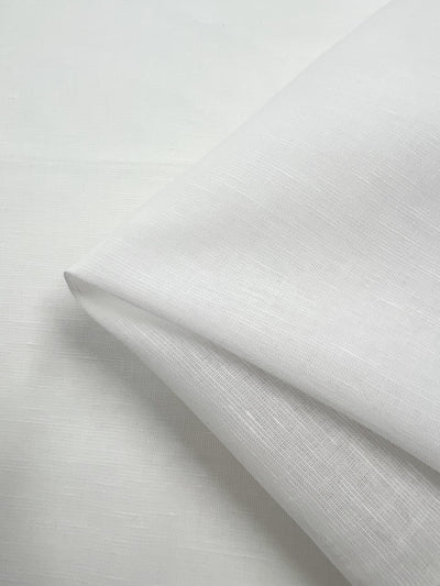 Close-up of a folded piece of Pure Linen Voile - White - 140cm from Super Cheap Fabrics, showcasing a textured weave. This Italian-sourced fabric is draped in layers, creating soft shadows and highlights that emphasize its smooth and slightly sheer quality.