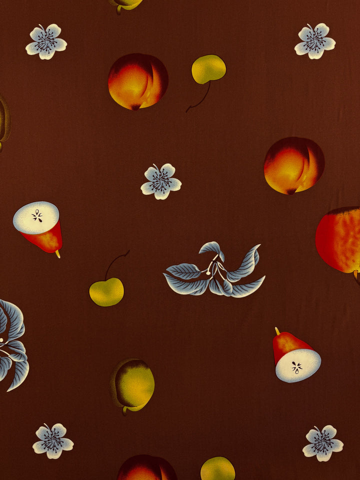 Designer Rayon - Orchard Pop by Super Cheap Fabrics features vibrant apples, pears, cherries, plums, and white flowers with blue leaves scattered on a dark brown background. 145cm wide versatile fabric.